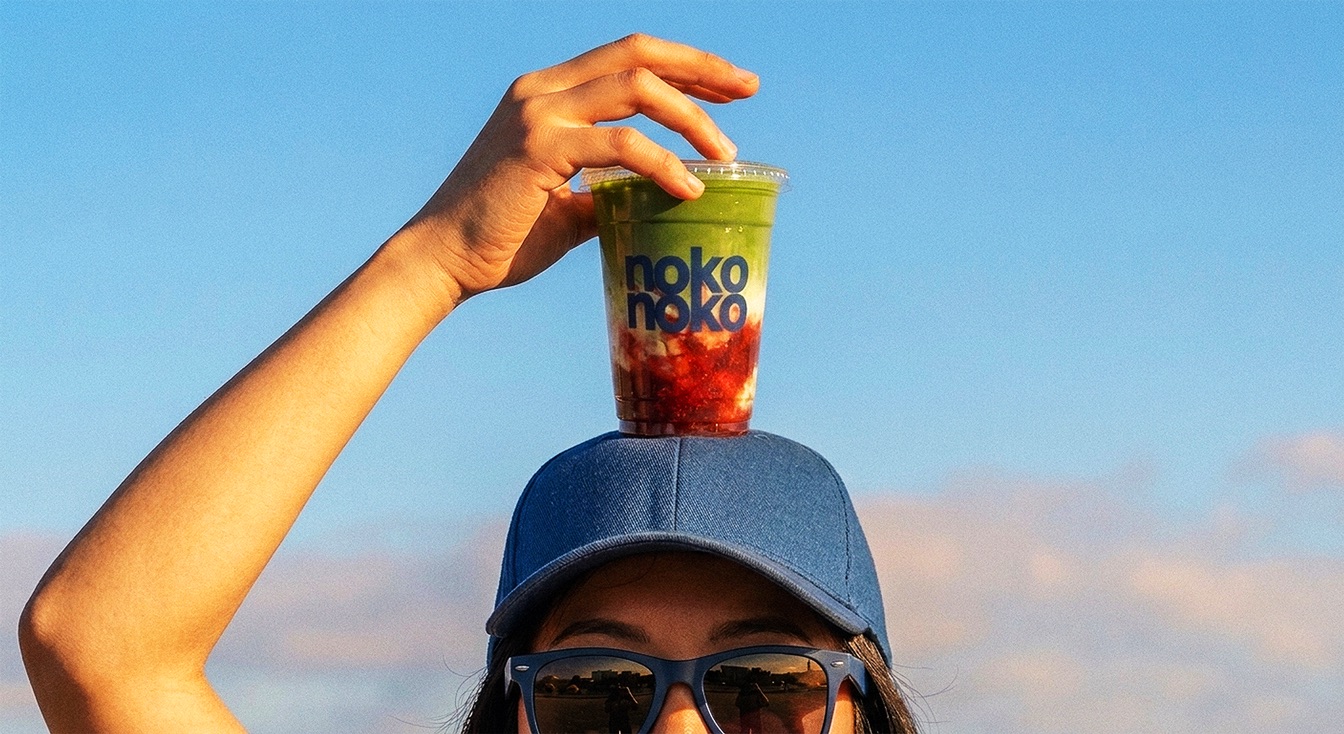 A hand balancing a nokonoko iced strawberry matcha on a denim cap against a blue sky